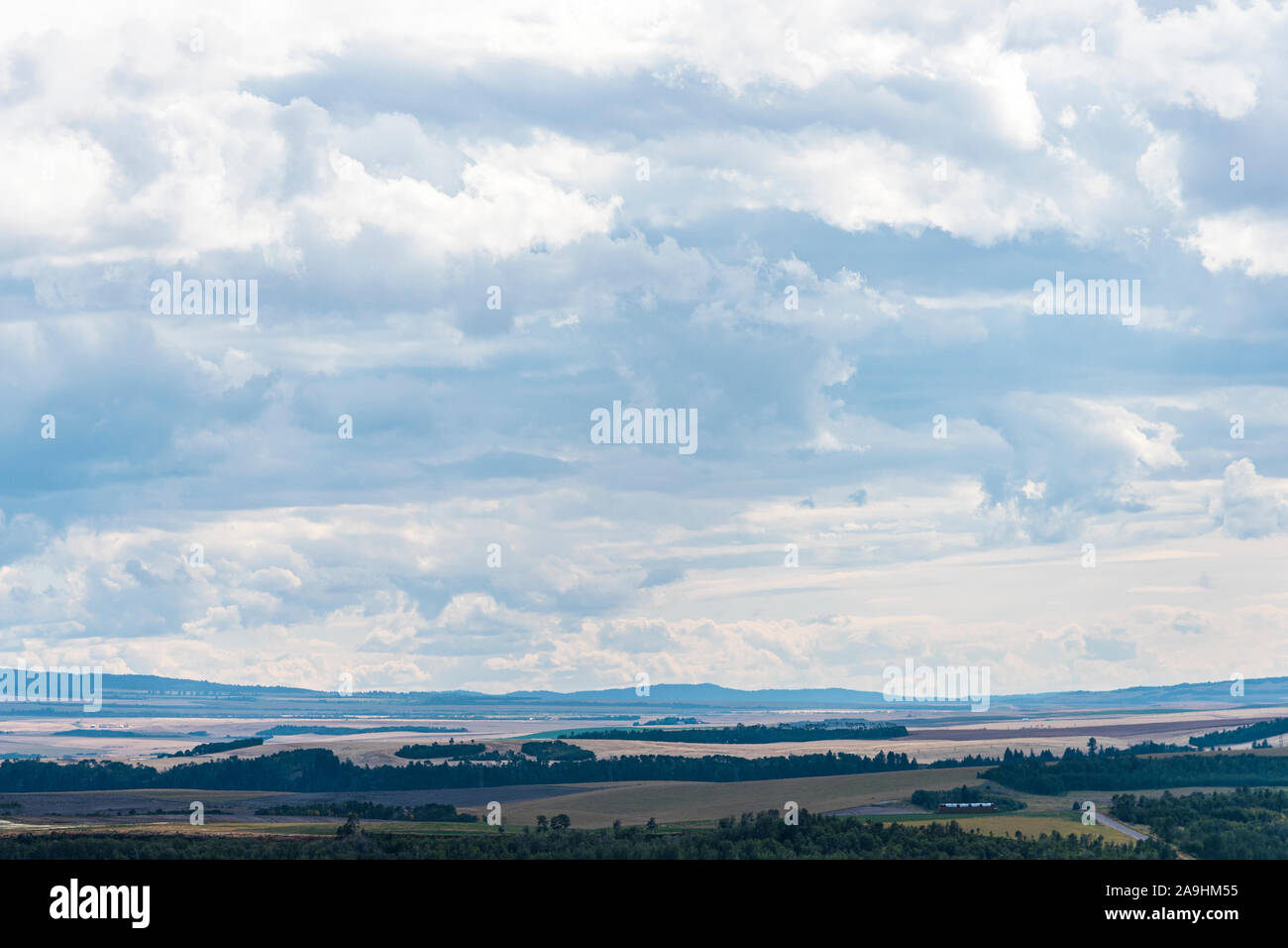 Blick über das Tal von Ackerland mit grünen Bäumen und duftigen Bergen unter bewölktem Himmel. Stockfoto