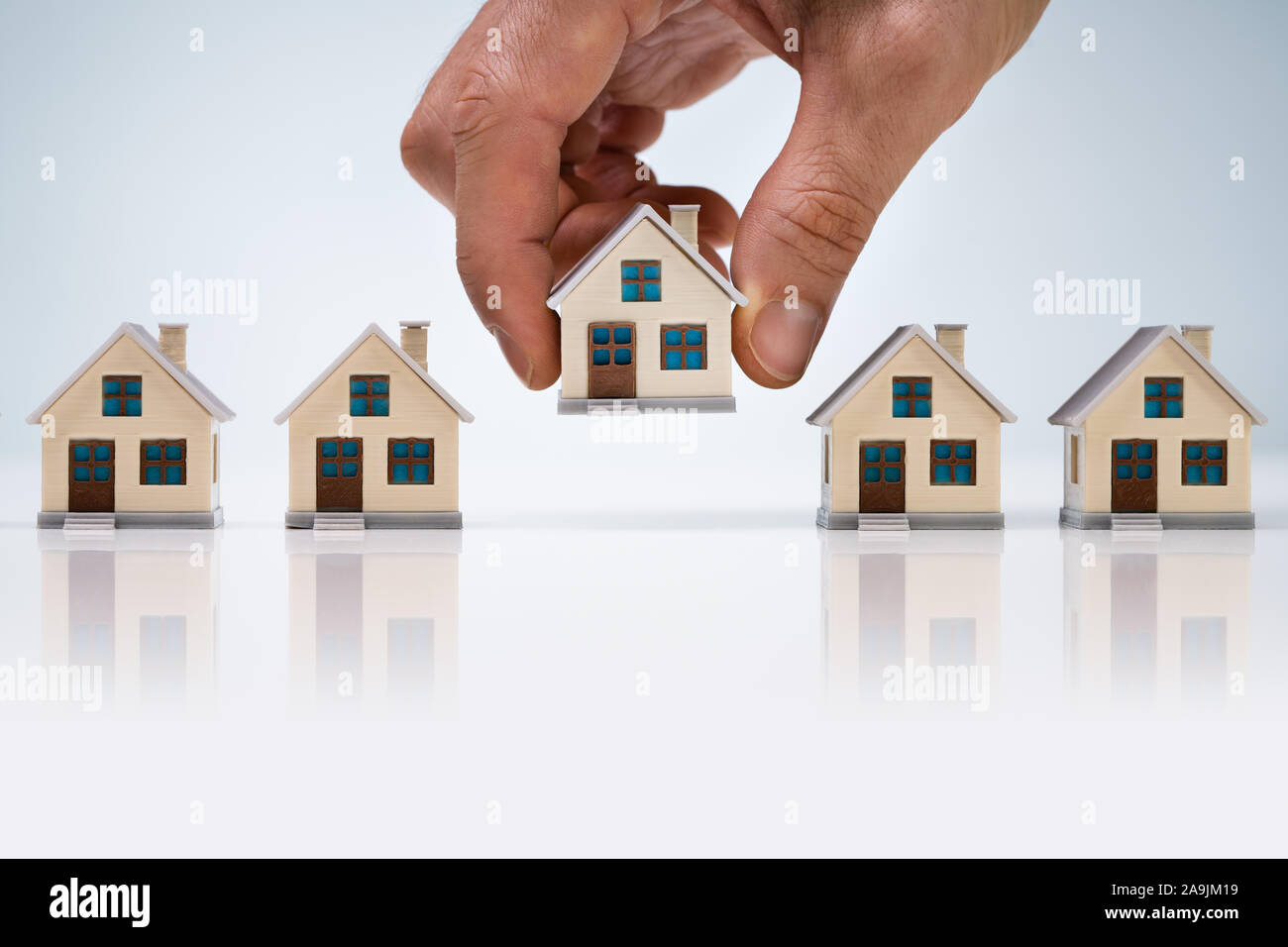 Person's Hand Wahl ein Haus Modell aus der Reihe über Weiß Schreibtisch Stockfoto