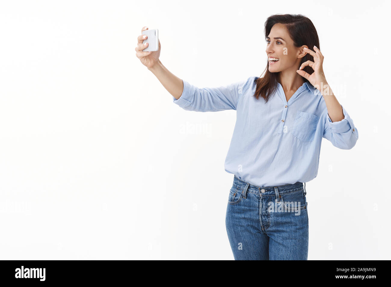 Gut gelaunt nach charmante Frau mit Tätowierungen tragen blaue Bluse, reden Ehemann online, halten Smartphones zeigen okay, Genehmigung unterzeichnen Handy Kamera, smil Stockfoto