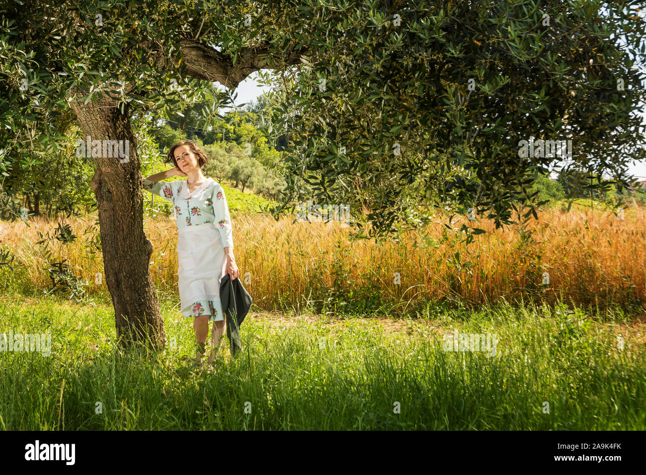 Frau in 40 die Kleider unter einem Olivenbaum in der Landschaft der Abruzzen mit einem Feld von Weizen im Hintergrund Stockfoto