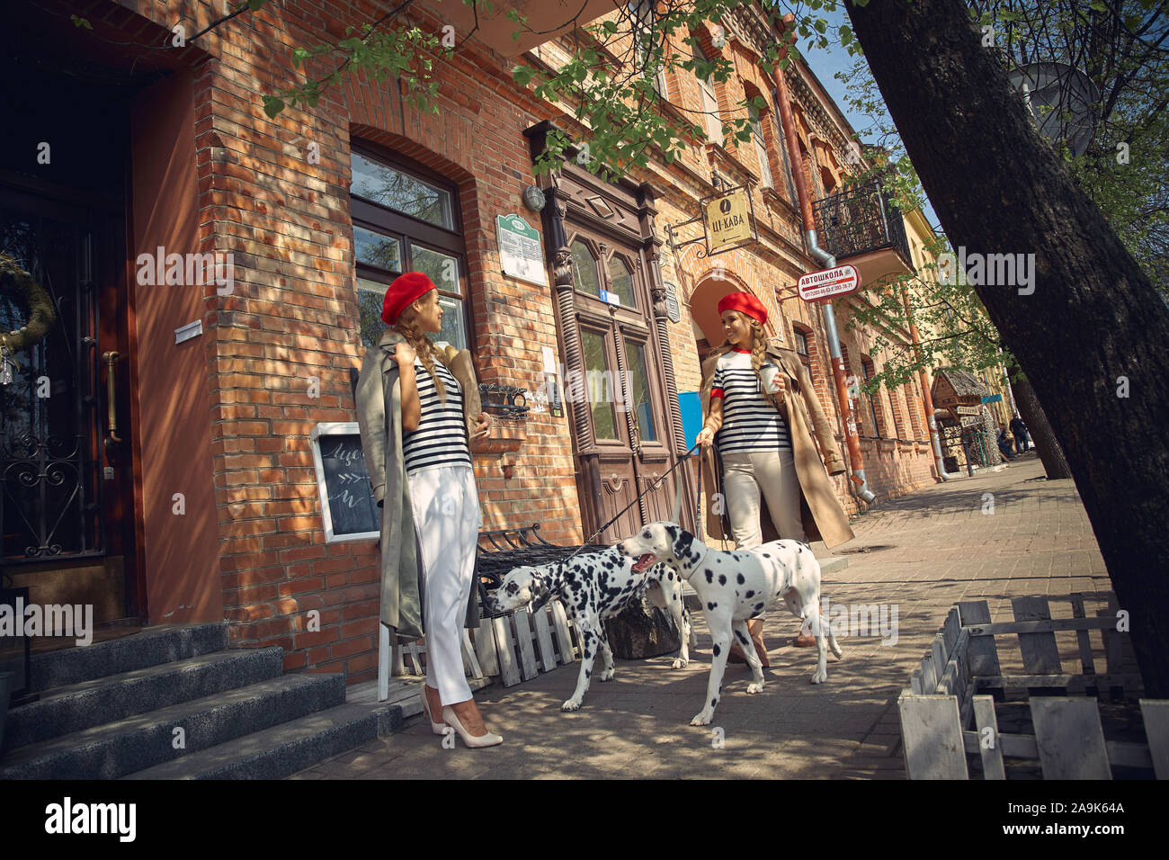 Zwei Mädchen in roten Barette sind Spaziergänge durch die Stadt mit Hunden der Dolmatian Rasse. Stockfoto