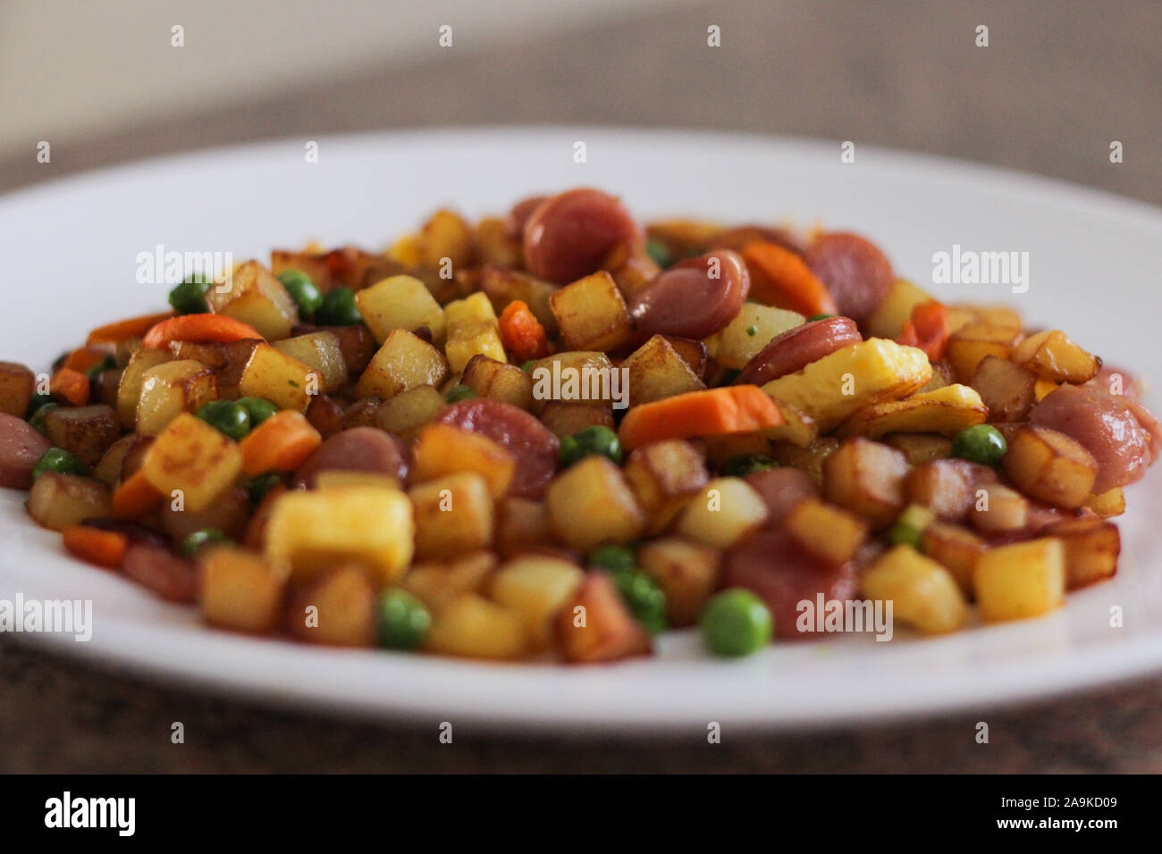 Beilage mit Omelette, Kartoffeln, Würstel, Karotten und Erbsen Stockfoto