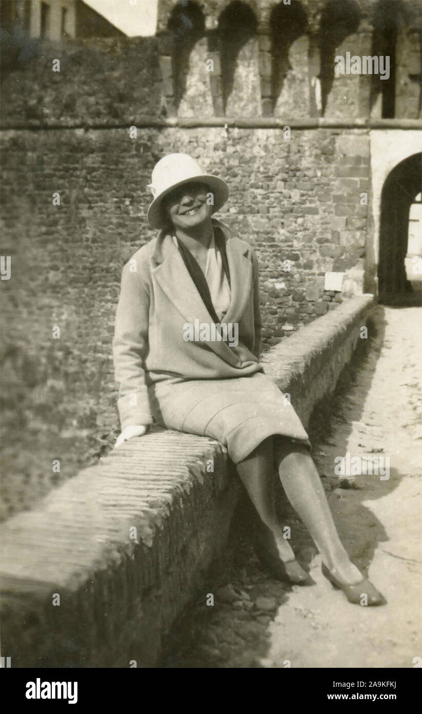 Eine Frau mit Hut und gestreifte Licht sitzen auf einer Mauer Mantel, Italien Stockfoto