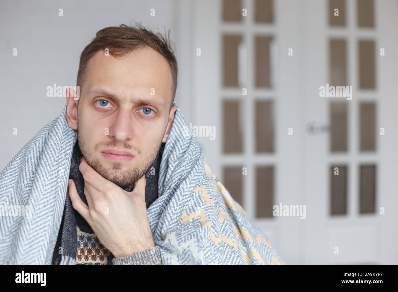Junger Mann mit Schal, den Kopf mit einer Decke zugedeckt, hält seinen Hals  wegen Halsschmerzen Stockfotografie - Alamy