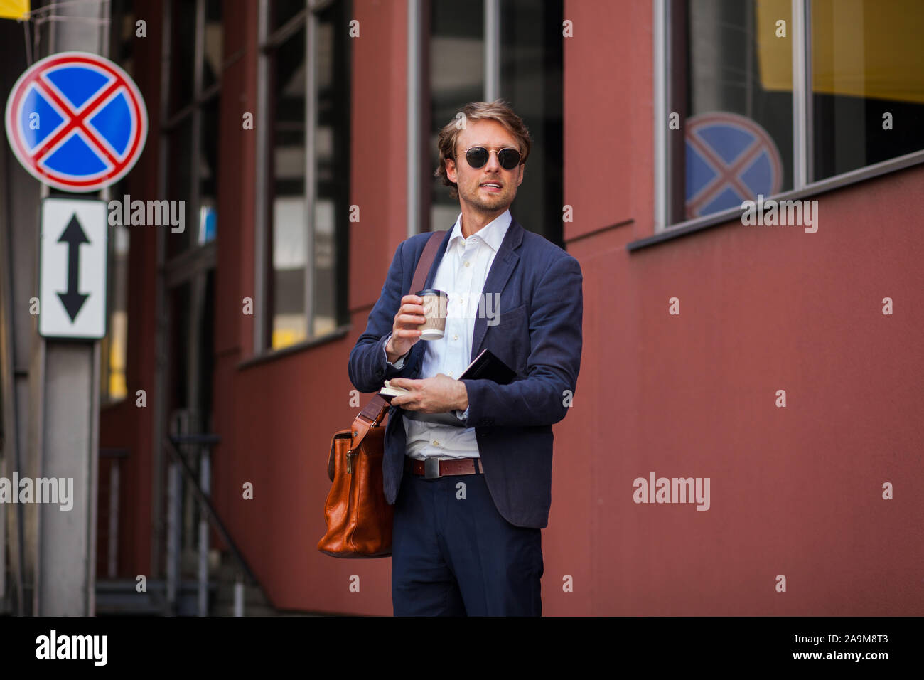 Attraktiver Mann in formelle Kleidung und Sonnenbrille ist seinen Kaffee im Freien genießen, in der Nähe des Amtes Stockfoto