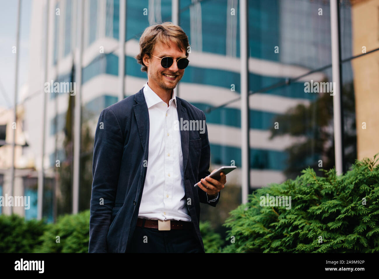 Die mittleren Manager in einem schönen stilvollen Anzug erhält positive Nachrichten über die Förderung bei der Arbeit in eine telefonische Nachricht Stockfoto