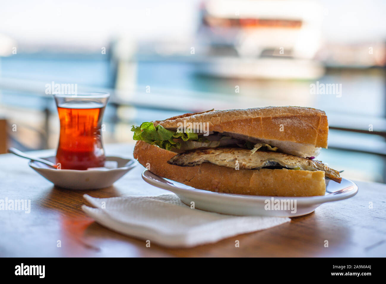 Istanbul fisch Sandwich. Burger mit gebratenen Fisch. Türkischer Tee mit Balik Ekmek. Unscharfer Hintergrund mit Meerblick Stockfoto