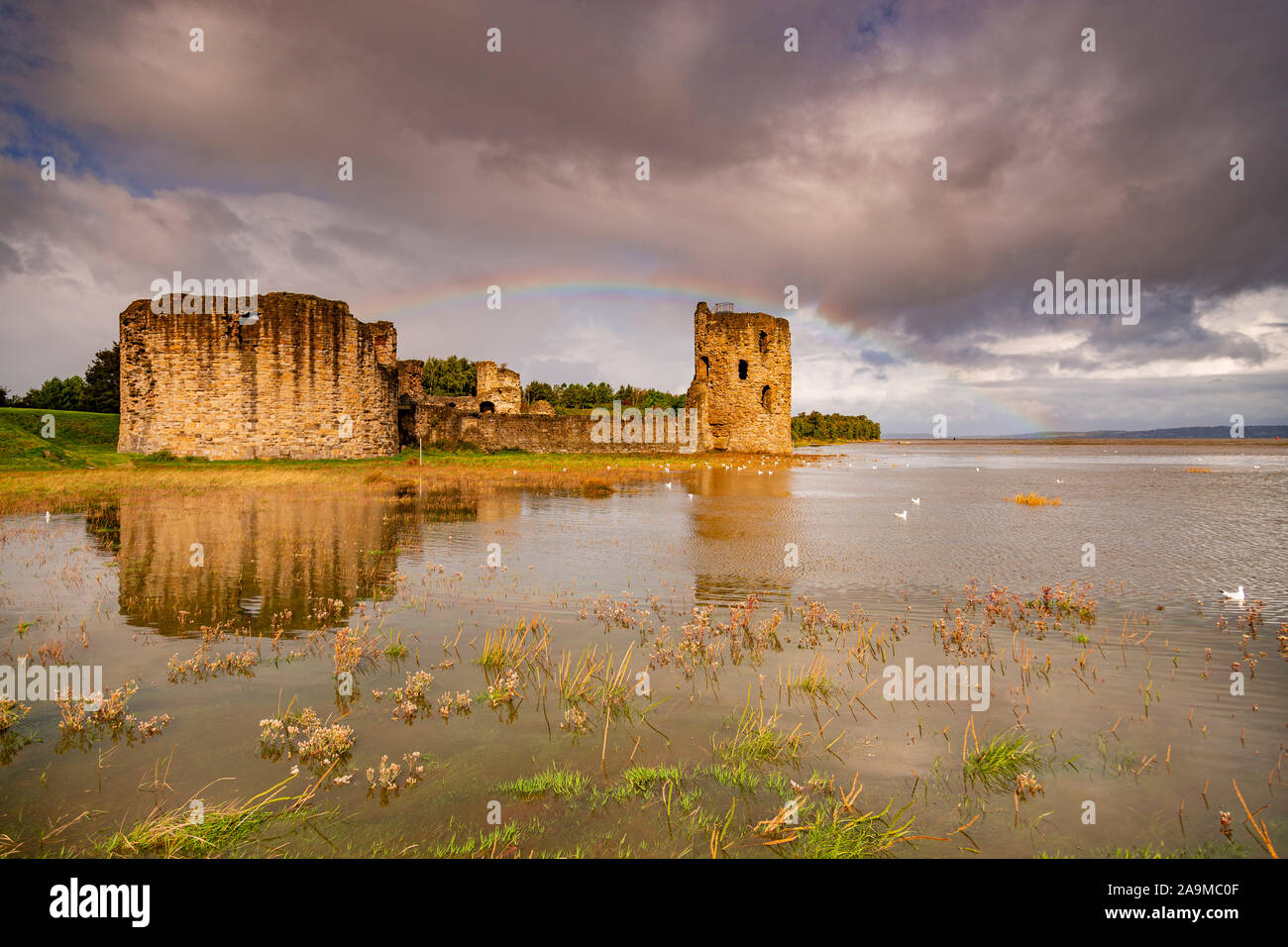 Flint Castle und Regenbogen bei Flut an der Küste von Nordwales Stockfoto