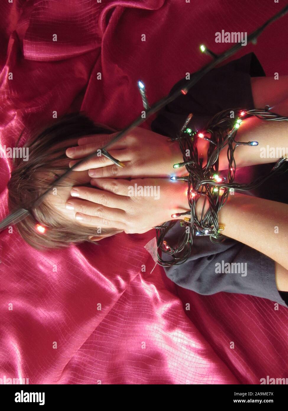 Junge bedeckte sein Gesicht mit beiden Händen durch Girlanden von Weihnachten l gebunden Stockfoto