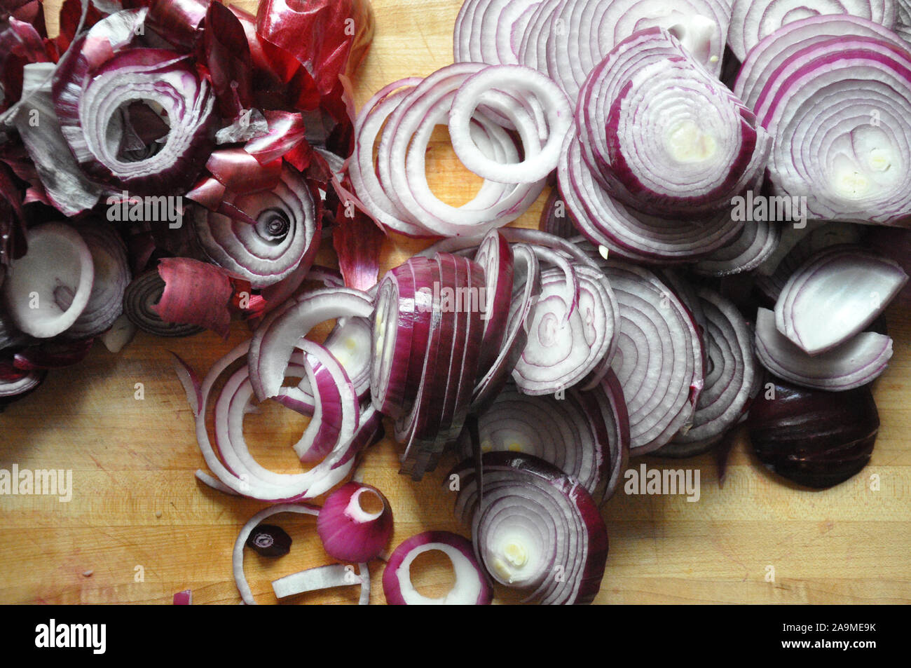 Rote Zwiebeln mit Skins auf der Seite auf einem hölzernen Schneidebrett in Scheiben geschnitten Stockfoto