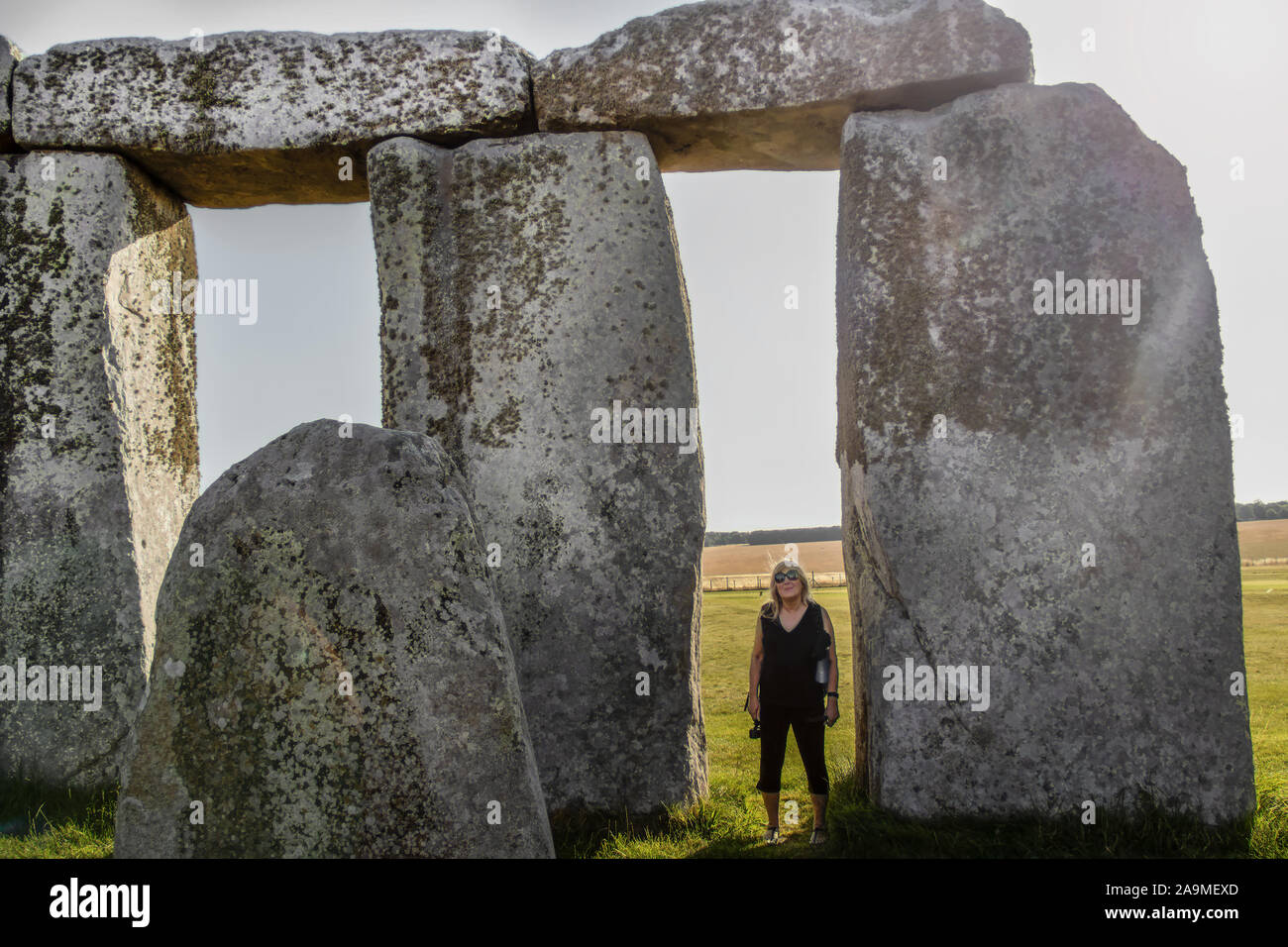 Touristische Frau, zwischen Steinen in Stonehenge in England an einem sonnigen Tag, um zu zeigen, wie groß sie sind, Stockfoto