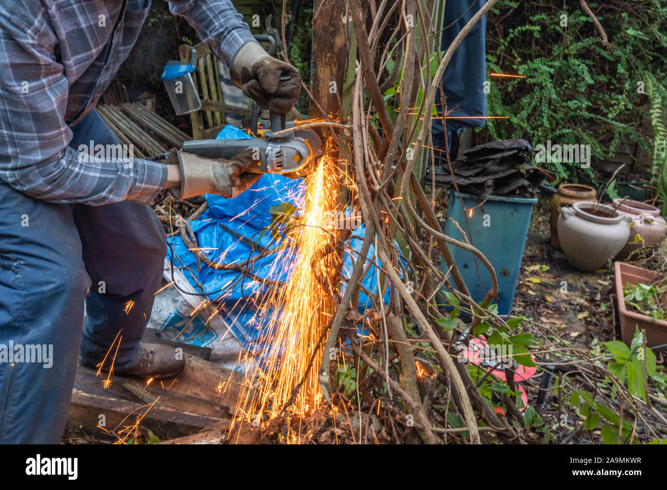 Mann mit einem Winkelschleifer im Garten arbeiten mit Funken fliegen. Abschneiden Gefährliche alte Nägel aus einem Post. Stockfoto