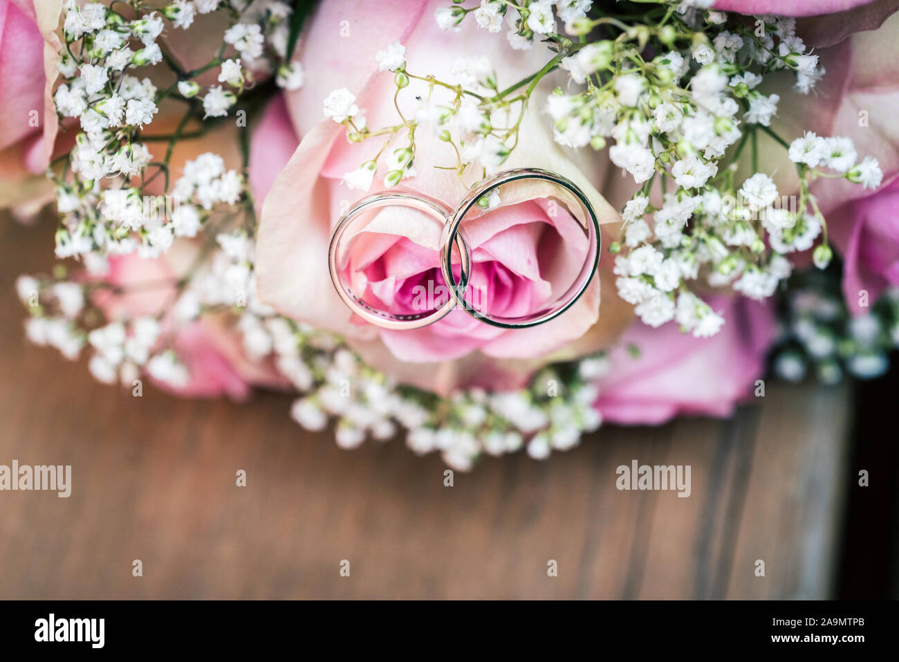 Wedding Bouquet mit rosa Rosen auf Holztisch mit Ringen. Hochzeit Ringe und schöne Hochzeit Strauß auf natürliche Holz Schreibtisch mit Natur in backgrou Stockfoto