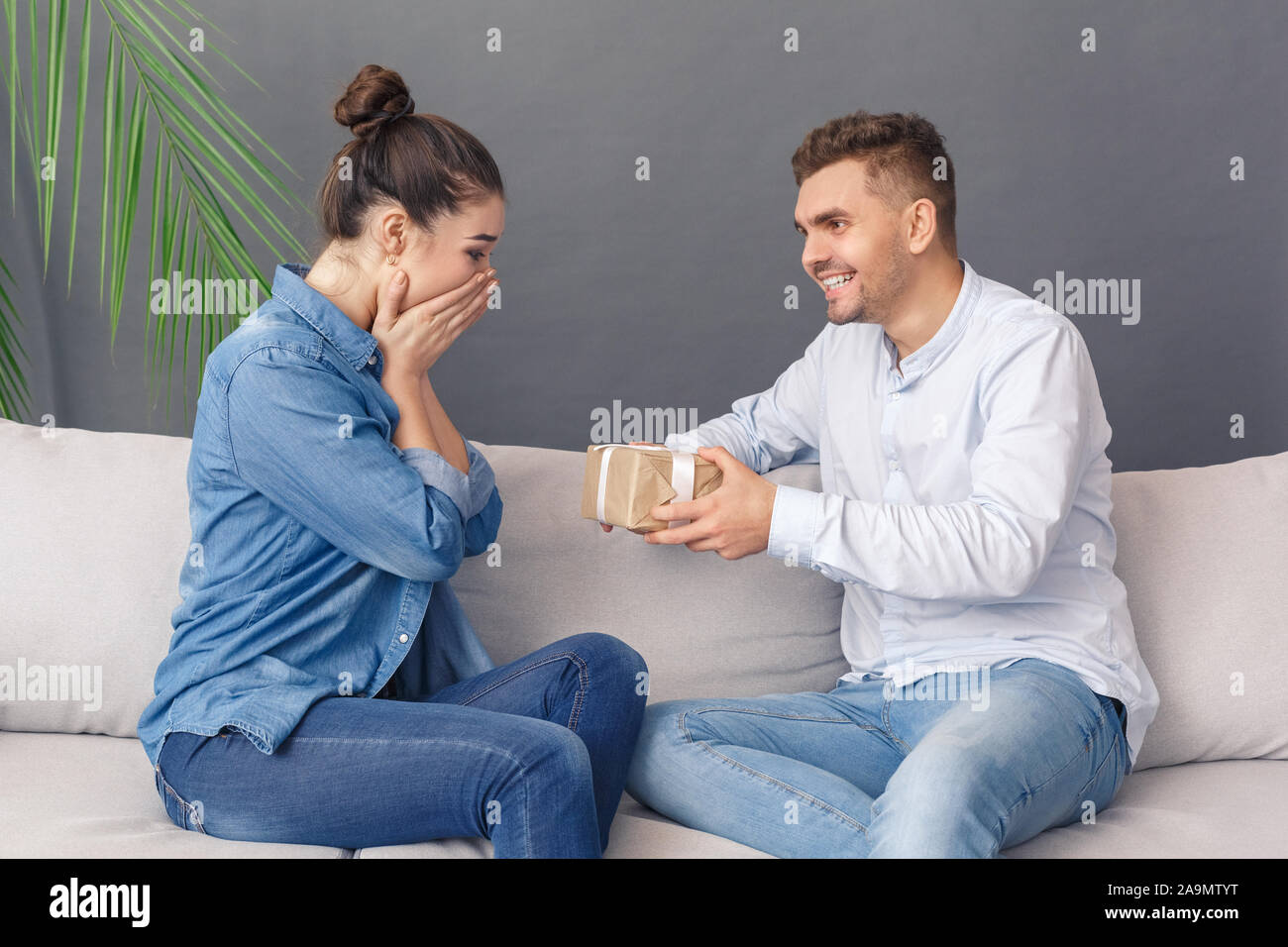 Urlaub Konzept. Junges Paar Mann zu Frau, Gesicht sitzen auf dem Sofa studio isoliert auf Grau berührt, Stockfoto