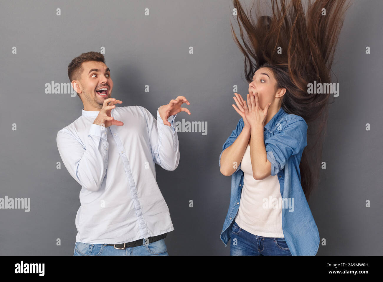 Spaß haben. Junges Paar Mann erschreckend Frau verspielt Studio stehen isoliert auf Grau Stockfoto