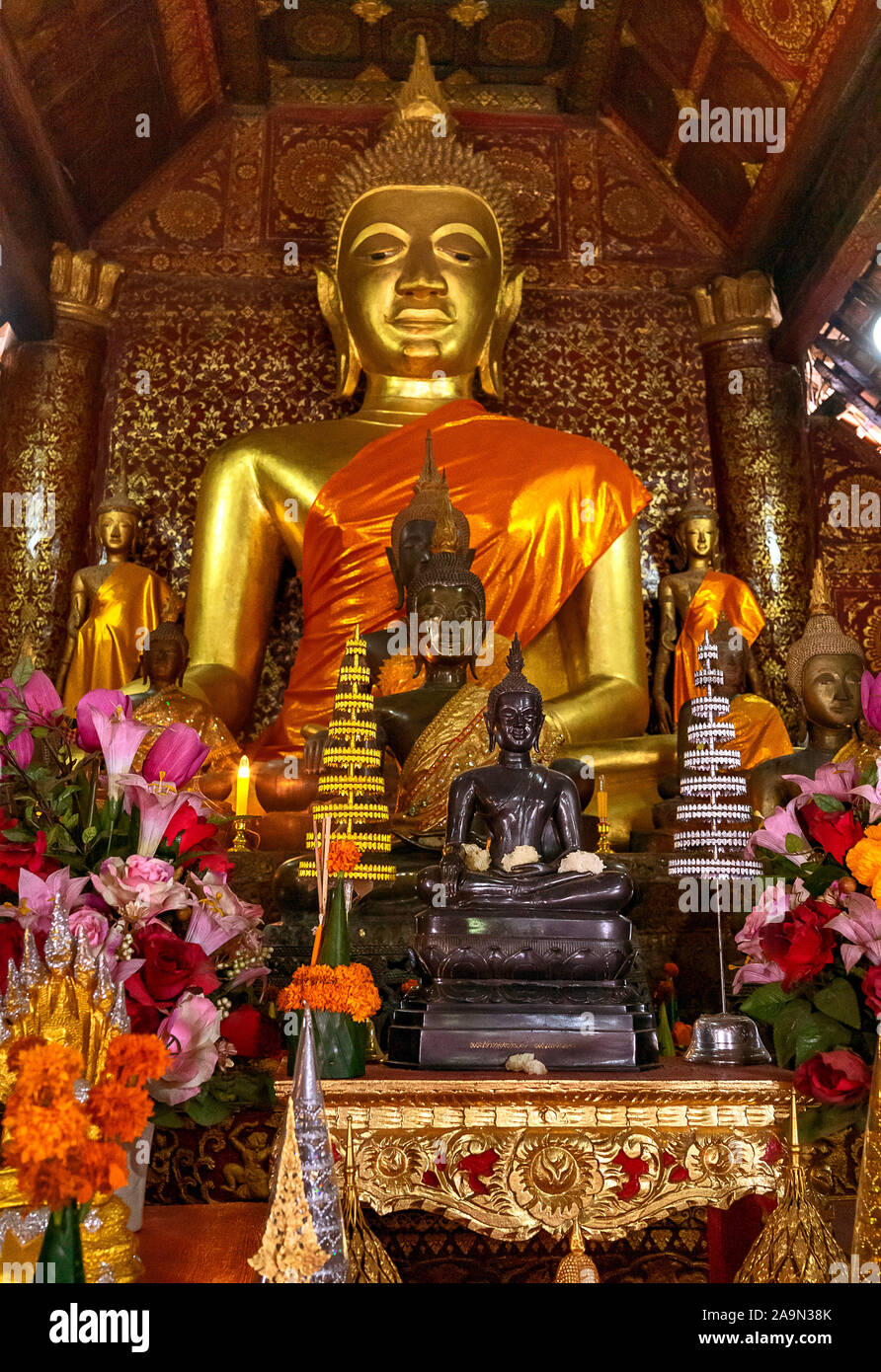 Buddha-Statuen und Blumenangebote in einem Tempel oder Wat in der malerischen Stadt Luang Prabang in Laos, die zum UNESCO-Weltkulturerbe gehört. Südostasien. Stockfoto