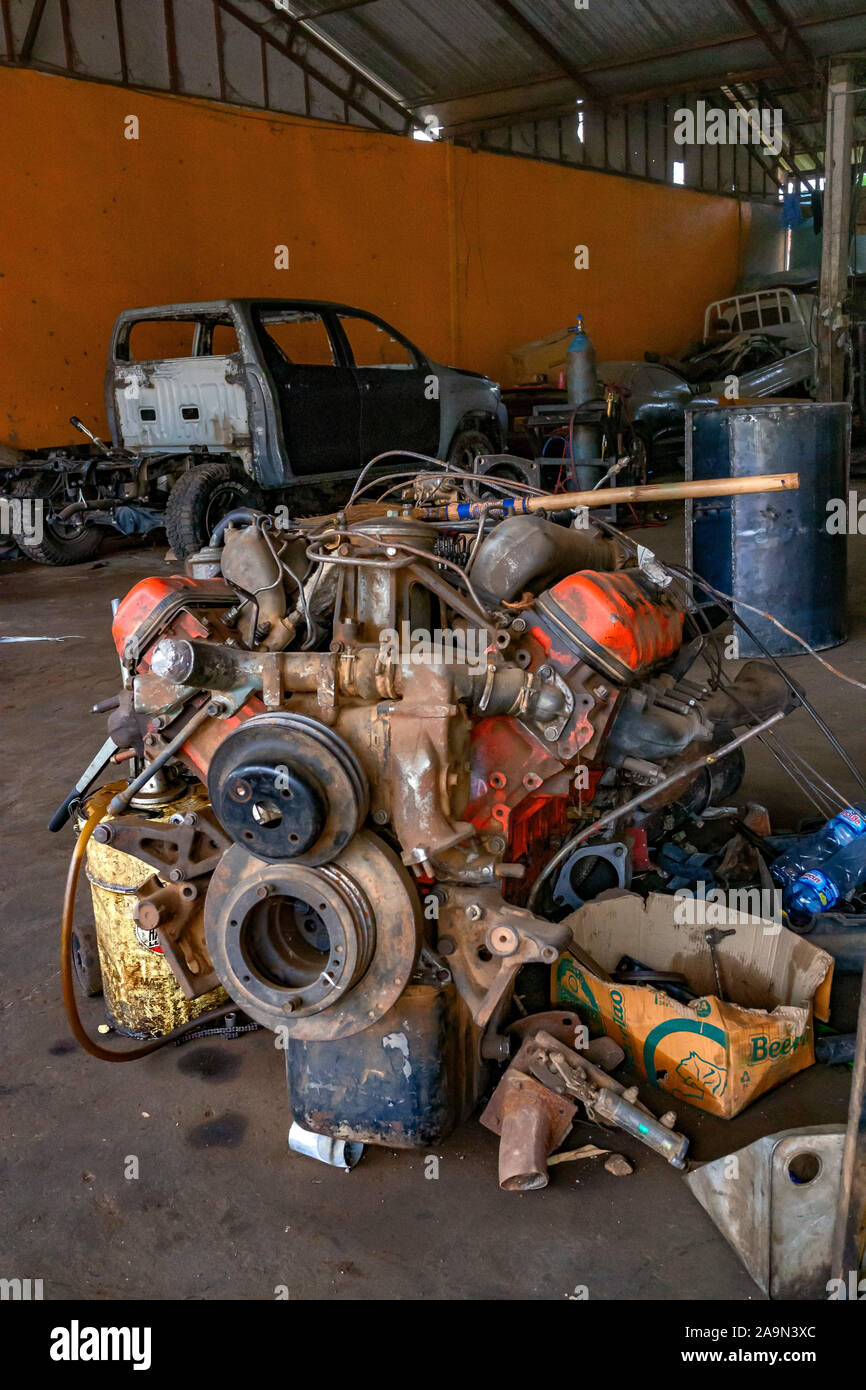 Eine Werkstatt für Motormechaniker in Luang Prabang Laos Südostasien. Im Vordergrund sitzt ein riesiger LKW-Motor auf dem Boden. Vertikales Format. Stockfoto