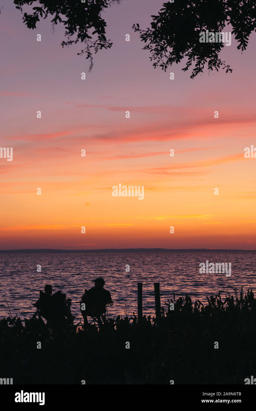 Die Silhouette eines Paar sitzt auf einem Dock beobachten die rosa Sonnenuntergang über See Apopka in Florida. Stockfoto