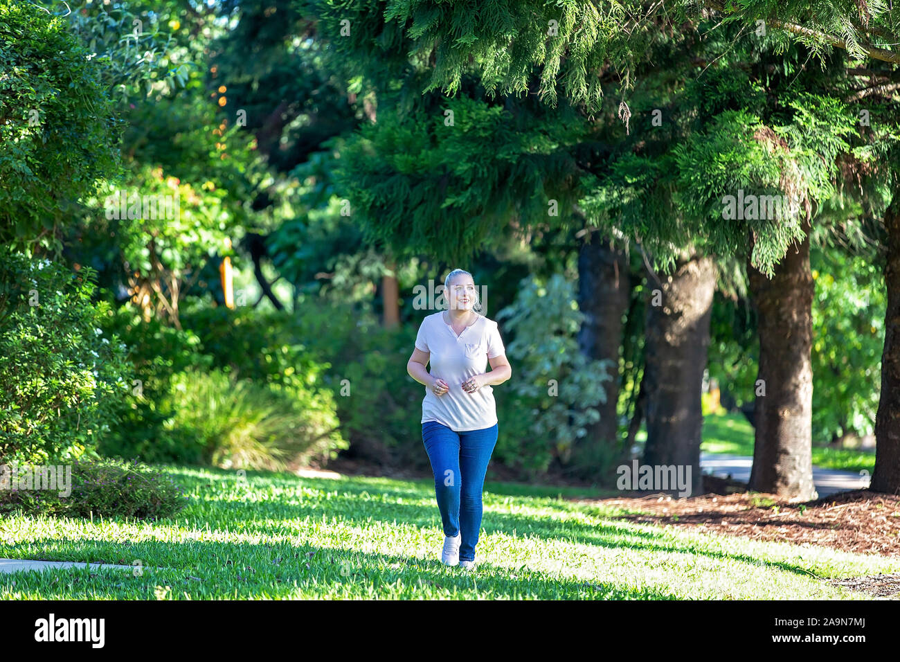 Frau joggen in botanischen Gärten mit späten Nachmittag Licht, das durch die Bäume Stockfoto