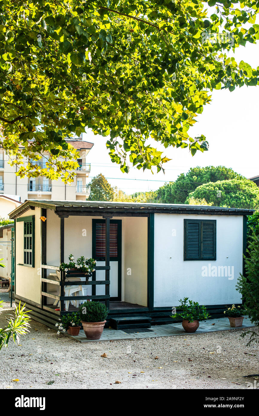 Kleine weiße Bungalow auf einem Campingplatz. Viele Bäume und Gasse auf Camping. Konzept für Erholung und Entspannung. Anreise und Unterkunft in der Natur. Kleine home Stockfoto