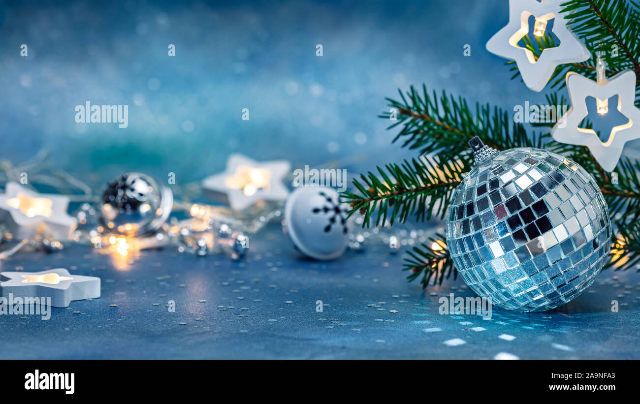 Silber glas kugel, Jingle bells und leuchtende Sterne leuchten Girlande. grüner Weihnachtsbaum Zweig auf unscharfen Hintergrund blau. Neues Jahr die Dekoration Stockfoto