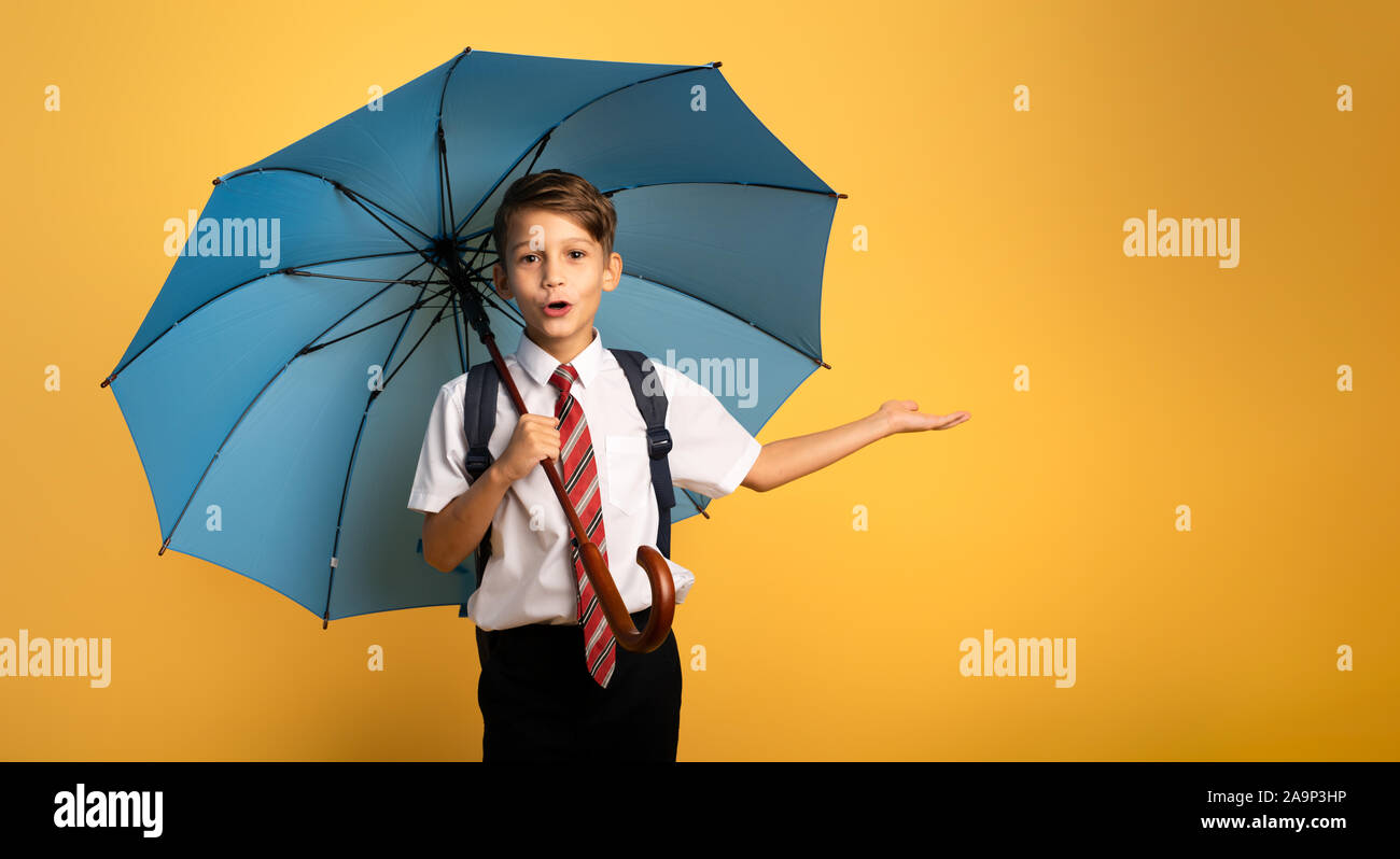 Kind student mit blauen Sonnenschirm auf gelben Hintergrund. Erstaunt Ausdruck Stockfoto