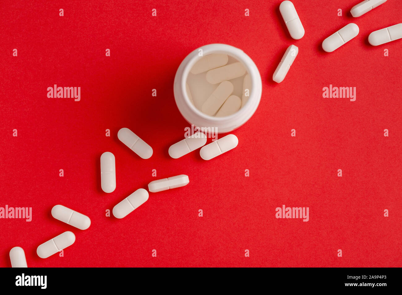 Weiße Pillen auf einem roten Hintergrund. Kunststoff weiß Medizin Flasche. Ansicht von oben Stockfoto