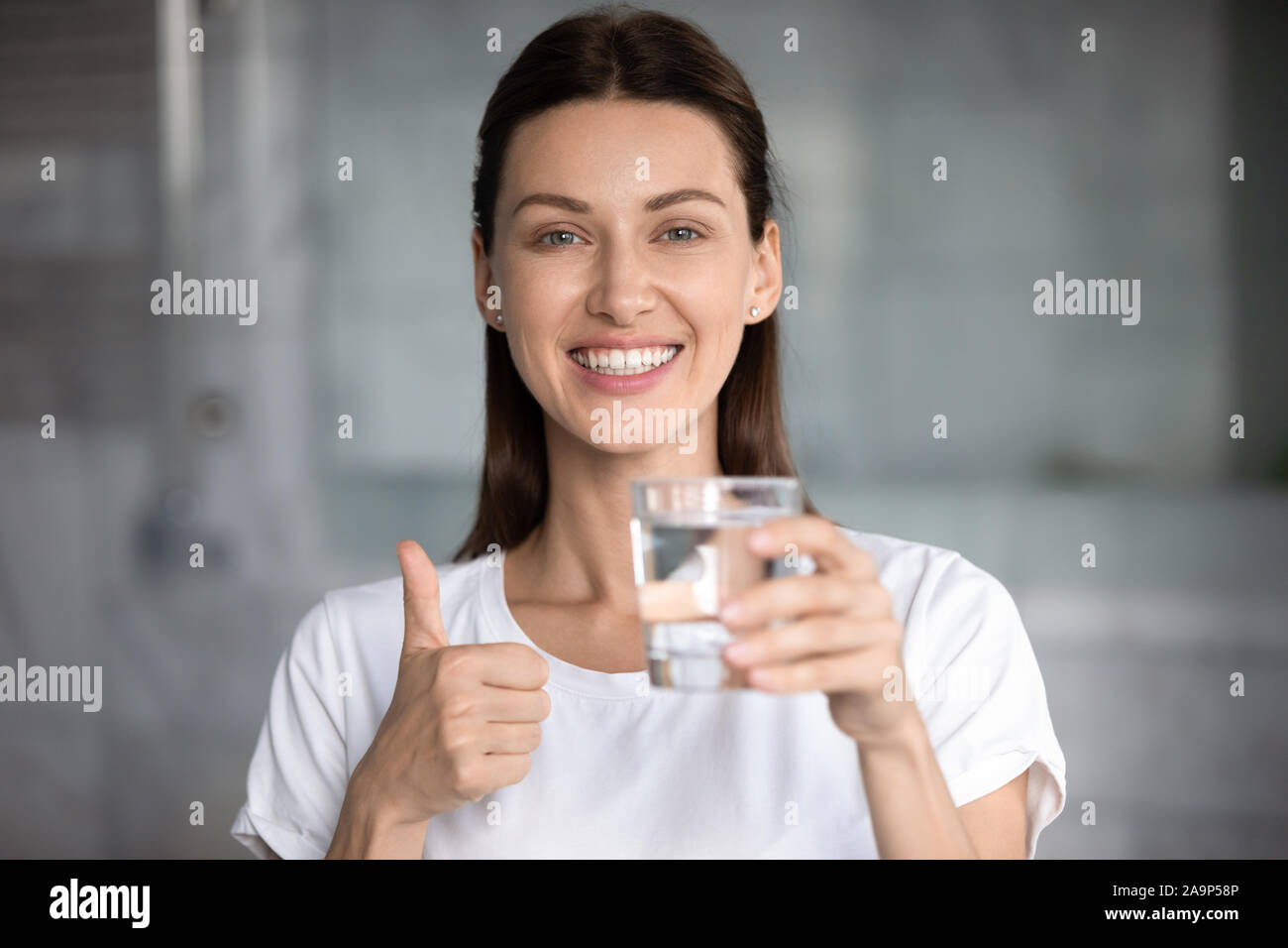 Gerne attraktive Frau hält Glas Wasser mit Daumen hoch Stockfoto