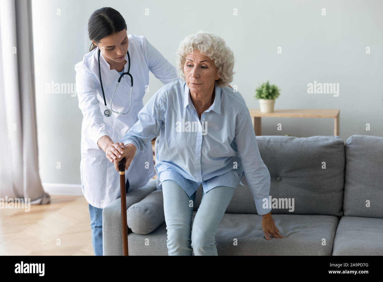 Krankenschwester helfen Oma von sofa Halten walking stick Stockfoto