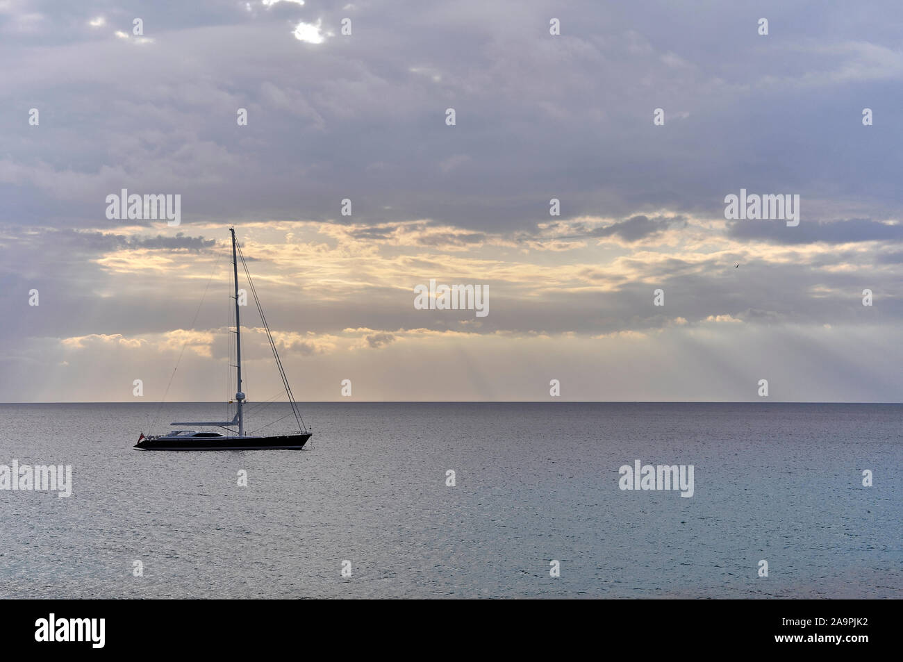 Luxus Segelschiff verankert bei Sonnenuntergang mit Wolken und Sonnenstrahlen in der Nähe von Cala Saona (Formentera, Pityuses, Balearen, Mittelmeer, Spanien) Stockfoto