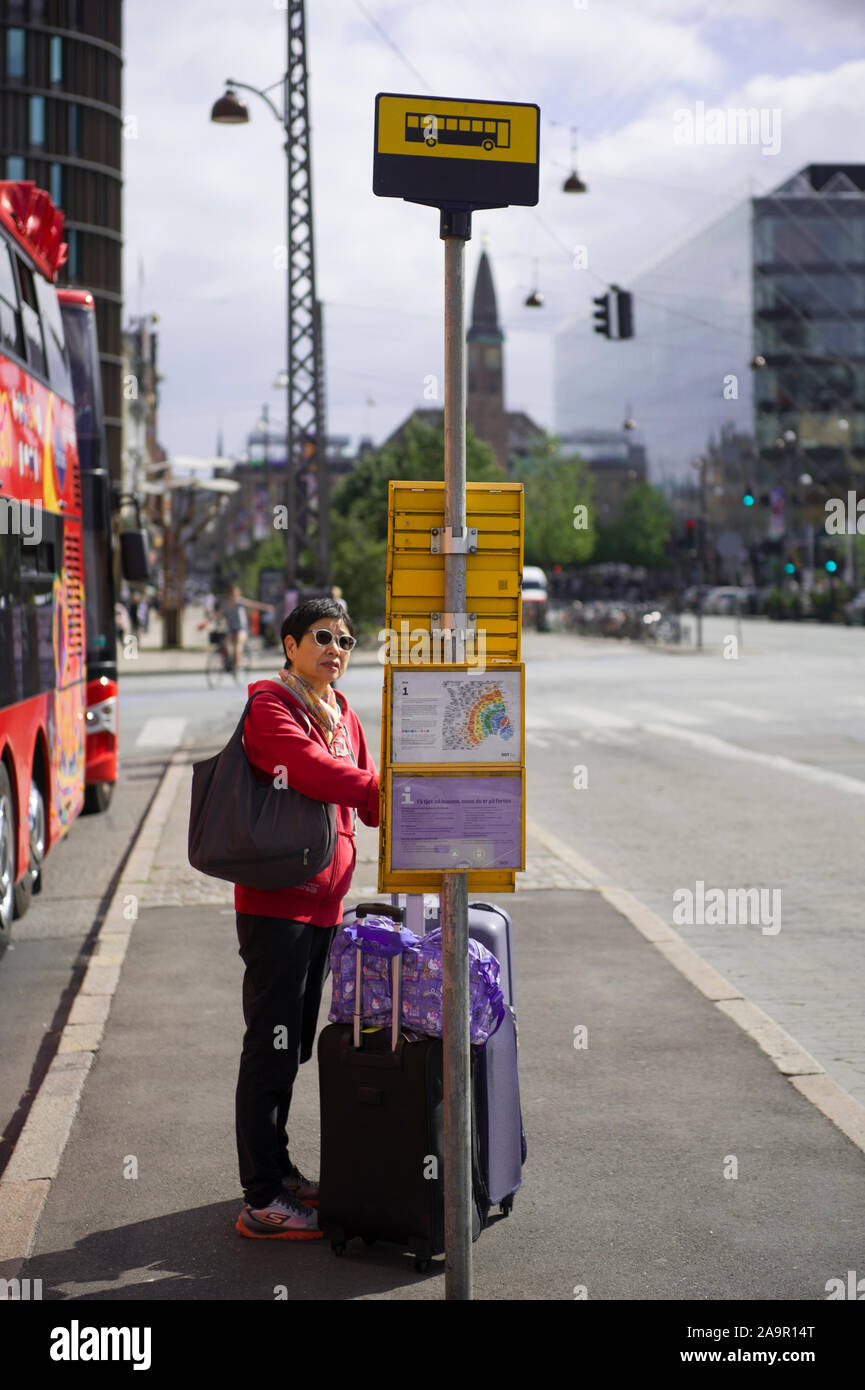 Eine Frau, die mit ihrem Koffer an einer Bushaltestelle in Kopenhagen, Dänemark warten Stockfoto