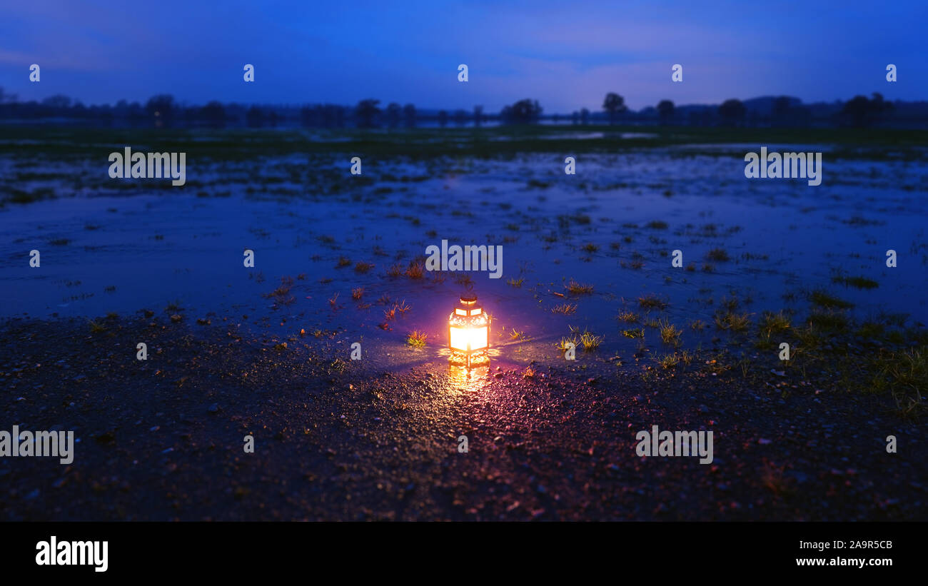 Eine reich verzierte Laternen leuchten am Abend nach Sonnenuntergang. Auf dem Boden, in Hochwasser in einem Feld in einem Winter Abend wider. Dunkle Landschaft Nacht Stockfoto