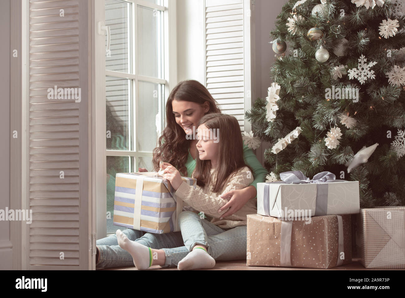 Glückliche Mutter und ihre kleine Tochter auspacken Geschenkbox in der Nähe der Weihnachtsbaum zu Hause Stockfoto