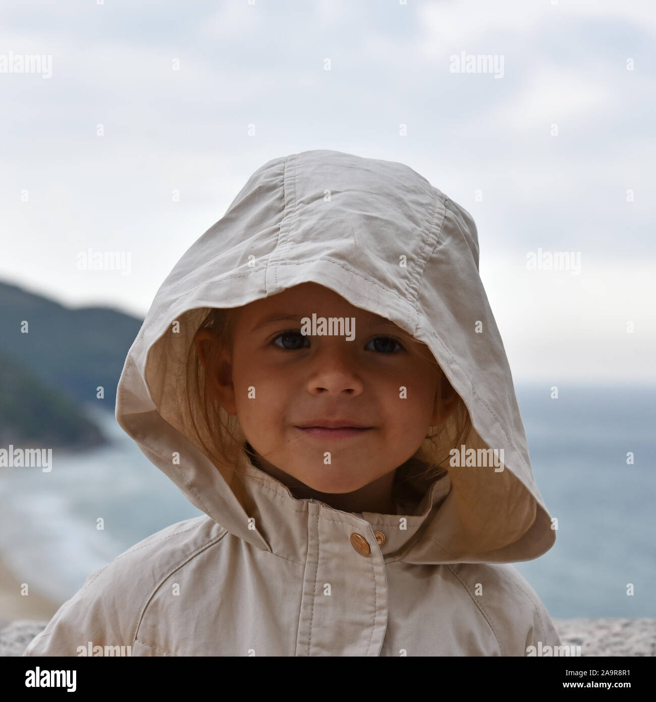 Ein kleines Mädchen trägt ein regenmantel Jacke mit Kapuze gegen einen stürmischen Himmel. Magnetische und intensiven Blick. Kindheit Konzepte. Ökologische Konzepte. Clim Stockfoto