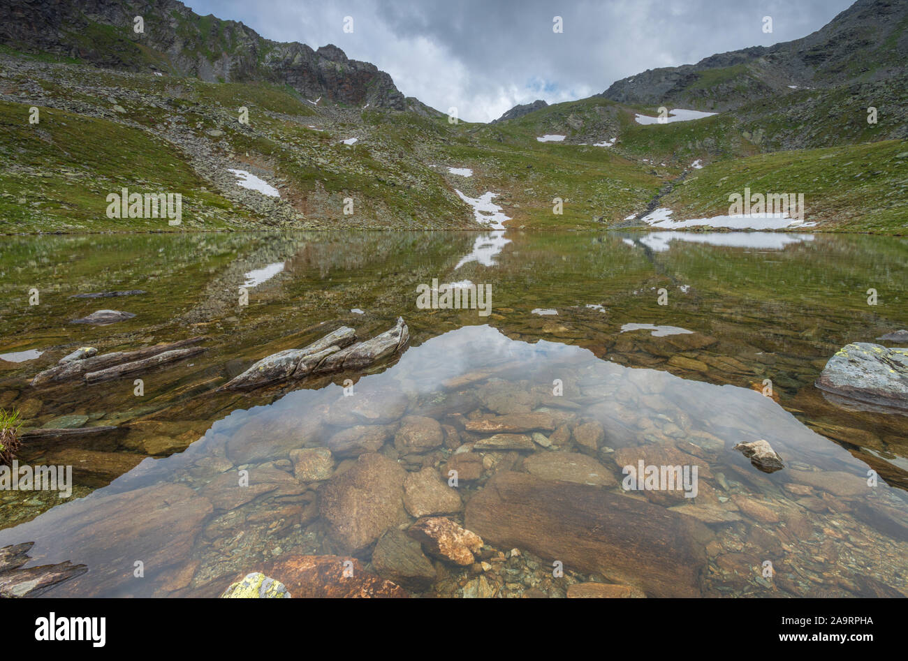 Kofler, Kofler See in die italienischen Alpen, kleine Emerald Lake mit felsigen Boden und dunklen Berge in der Umgebung. Grassy lake Banken. Stockfoto