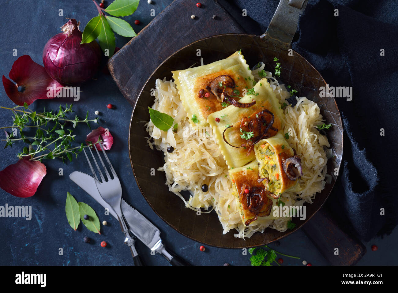 Gebratene schwäbische Gemüse Ravioli mit gerösteten Zwiebeln und Sauerkraut in eine eiserne Pfanne serviert pan Stockfoto