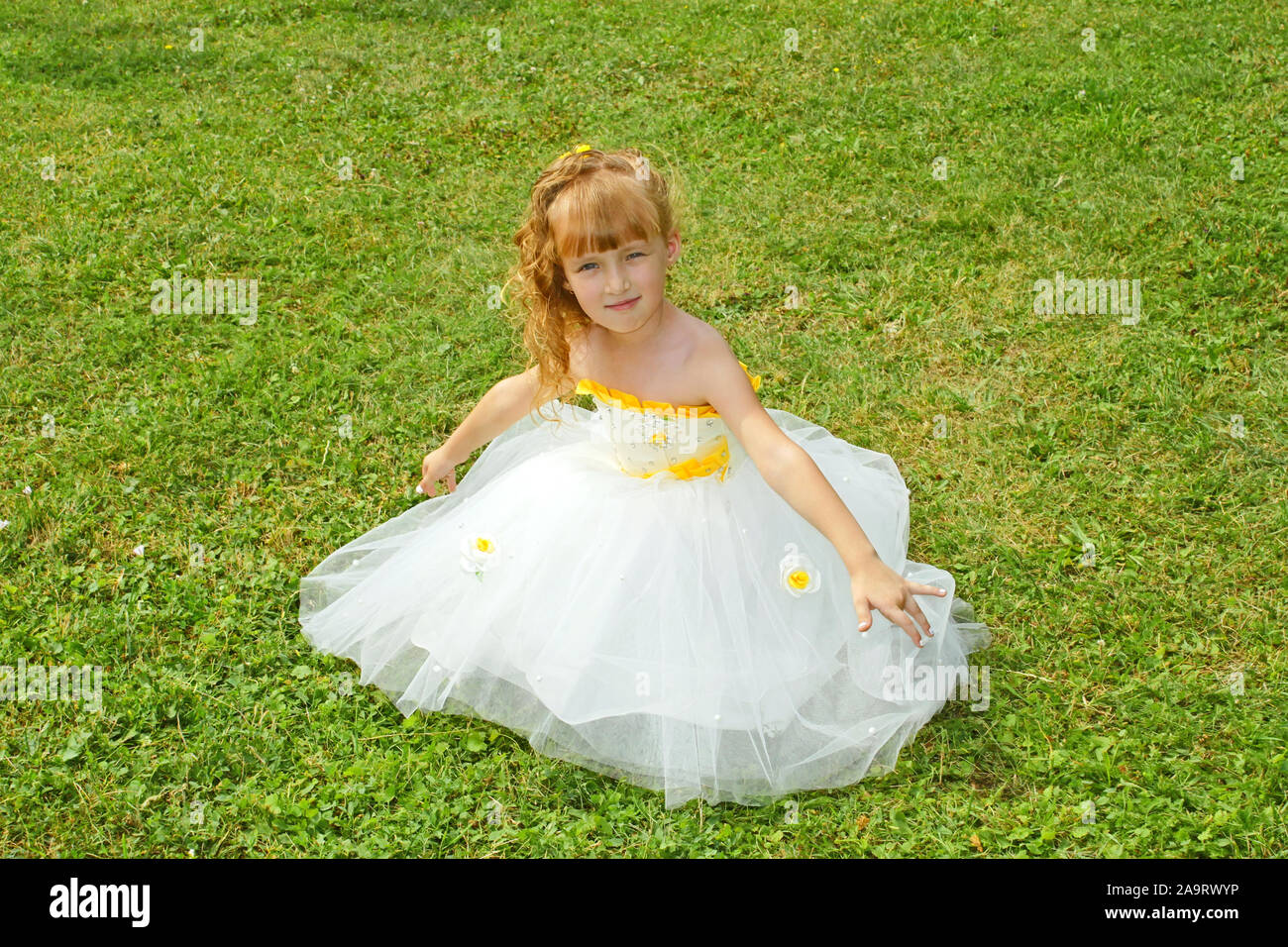Kleines Mädchen in einem gelben festliches Kleid auf einem grünen Rasen Stockfoto