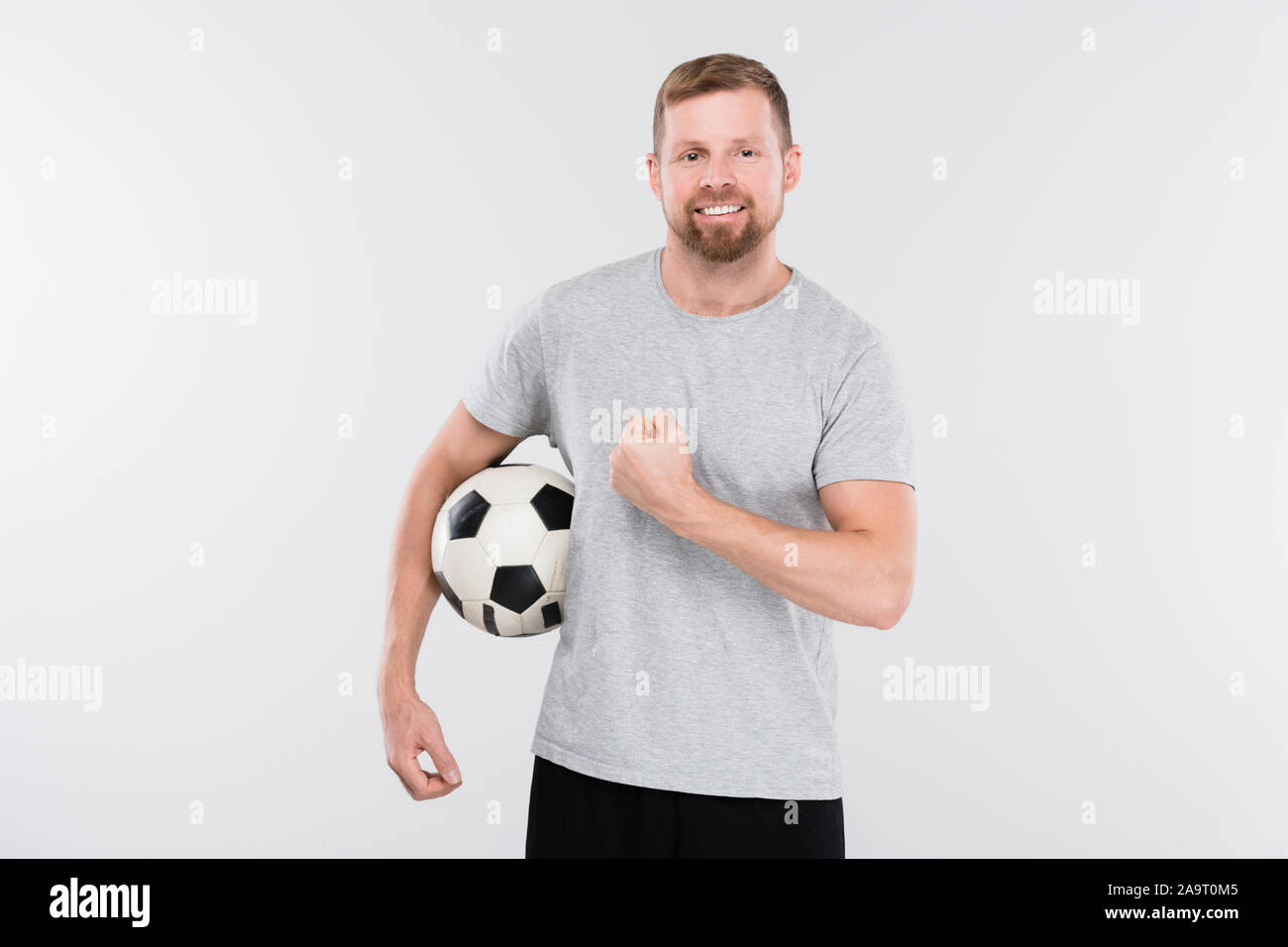 Junge erfolgreiche Fußball-Spieler in Sportkleidung holding Ball und zeigt Stärke Stockfoto