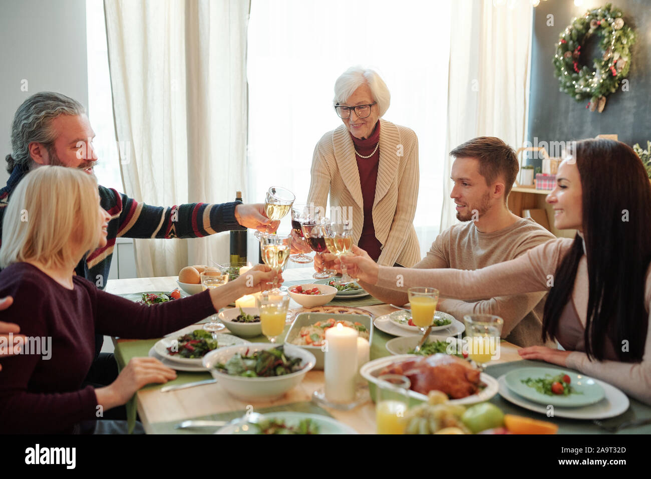 Junge und ältere Mitglieder der großen Familie klirren mit Gläsern Wein zum Abendessen Stockfoto