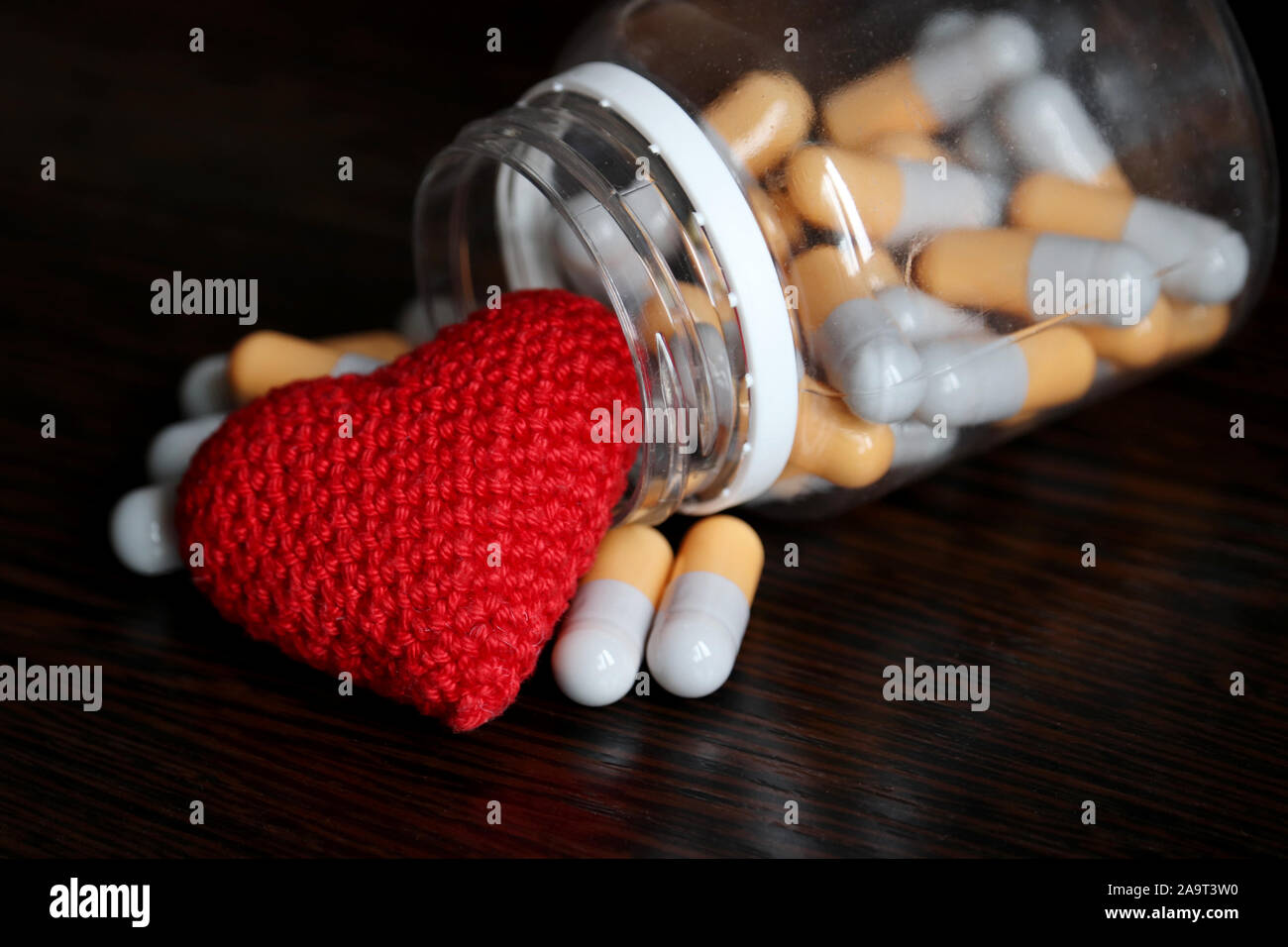 Pillen und gestrickten roten Herzen auf dunklen Holztisch, Flasche mit Medikamenten in Kapseln. Konzept der Hypertonie, Herzinsuffizienz, Kardiologie, Blut Stockfoto