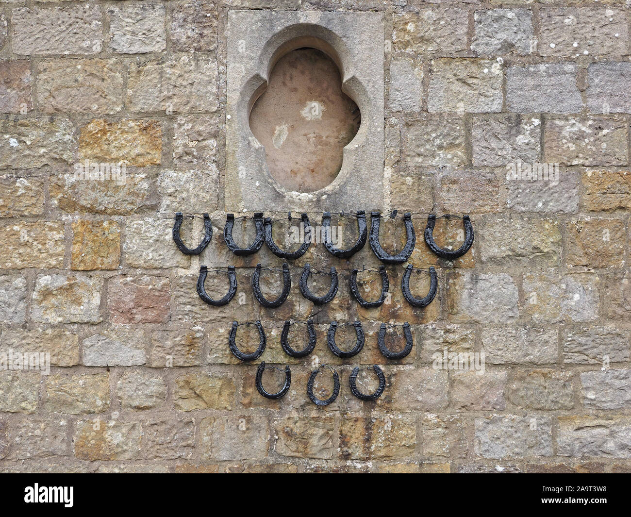 Sammlung von historischen Pferd - Schuhe schwarz lackiert & angezeigt in dreieckiger Anordnung (mit zwei Reihen fehlt) auf einer steinernen Burg Mauer in England, Großbritannien Stockfoto
