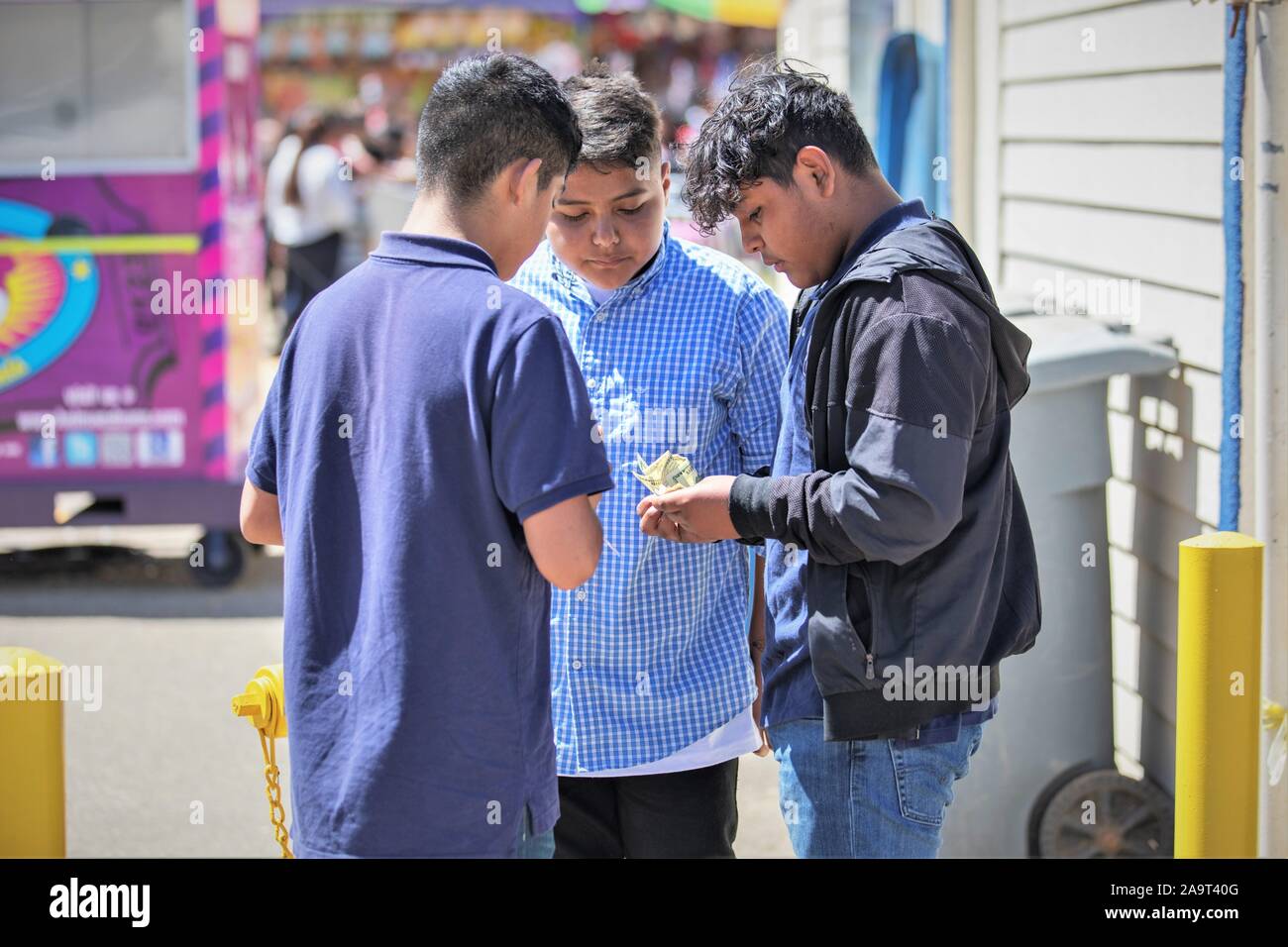 Drei jugendlich ethnischen junge Freunde Hispanic Jungs ihr Geld zählen für fair Kaufen ride Tickets an den lokalen Vergnügungspark Stockfoto