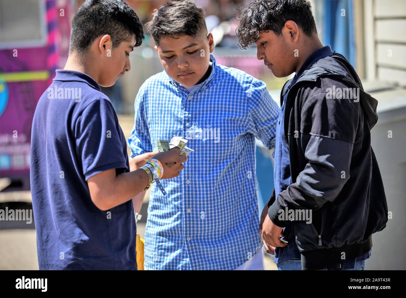 Drei jugendlich ethnischen junge Freunde Hispanic Jungs ihr Geld zählen für fair Kaufen ride Tickets an den lokalen Vergnügungspark Stockfoto