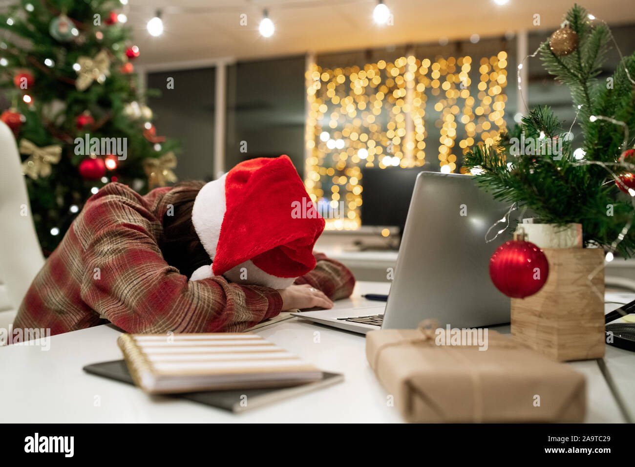 Erschöpft junge geschäftsfrau in Santa Kappe schlafen am Schreibtisch vor Laptop Stockfoto