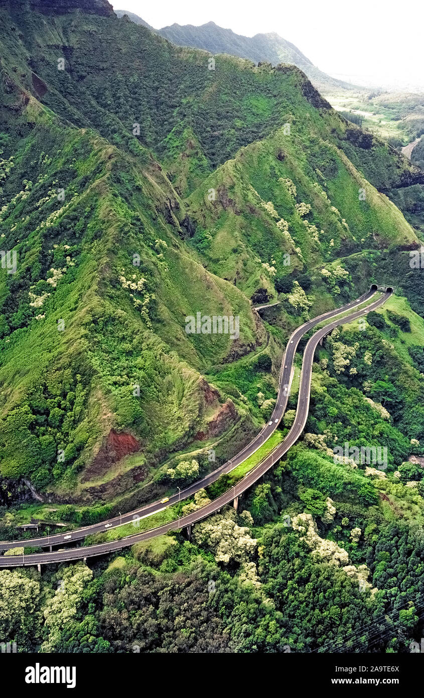 Der Pali Highway (Route 61) ist eine hauptdurchgangsstraße, die steilen grün bewaldeten Bergen Honolulu auf der Leeward Coast in Kailua auf der Luv Küste von Oahu, einer der acht großen Inseln im Pazifischen Ozean, die Teil der tropischen Hawaii, USA zu verbinden. Diese luftaufnahme zeigt eine erhöhte Abschnitt der vierspurigen Fahrbahn, geteilt durch den Twin Nuʻuanu Pali Tunnels geht in die Klippen gelangweilt. Die Autobahn wurde im Jahr 1959 eröffnet und folgt eine Route ähnlich der ersten Straße durch diese Koʻolau Mountain Pass in 1845 gebaut. Stockfoto