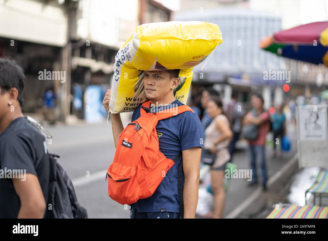 Eine junge Filipino Mann gleicht einem 50 kg Sack Reis auf seinem Kopf während der Wartezeit für die öffentlichen Verkehrsmittel. Stockfoto