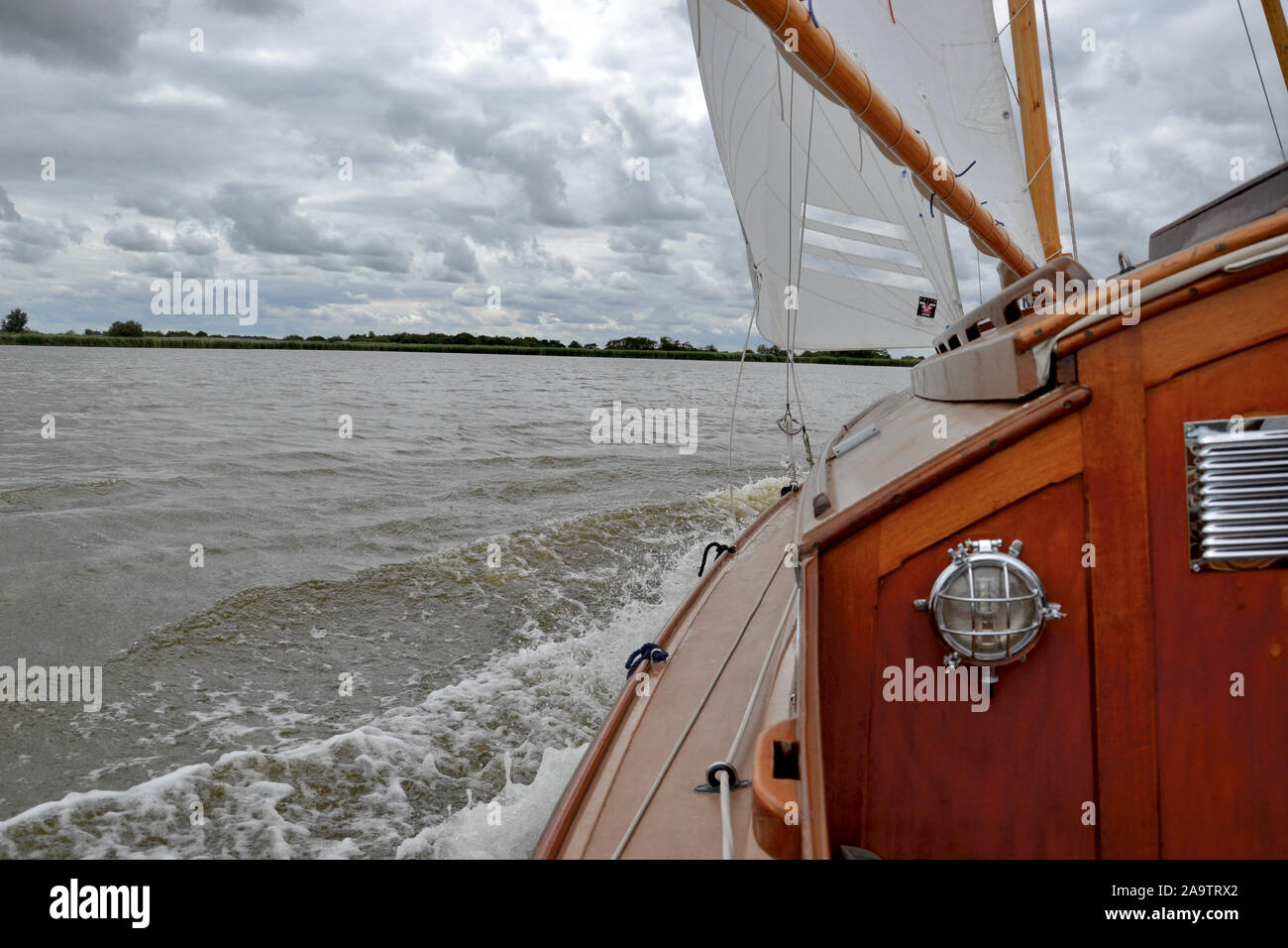 Blick aus dem Cockpit eines alten Holzhütte Yacht segeln schnell auf einem See an einem windigen, grauer Tag. Wellen blubbern um sidedeck, Segel voll. Stockfoto