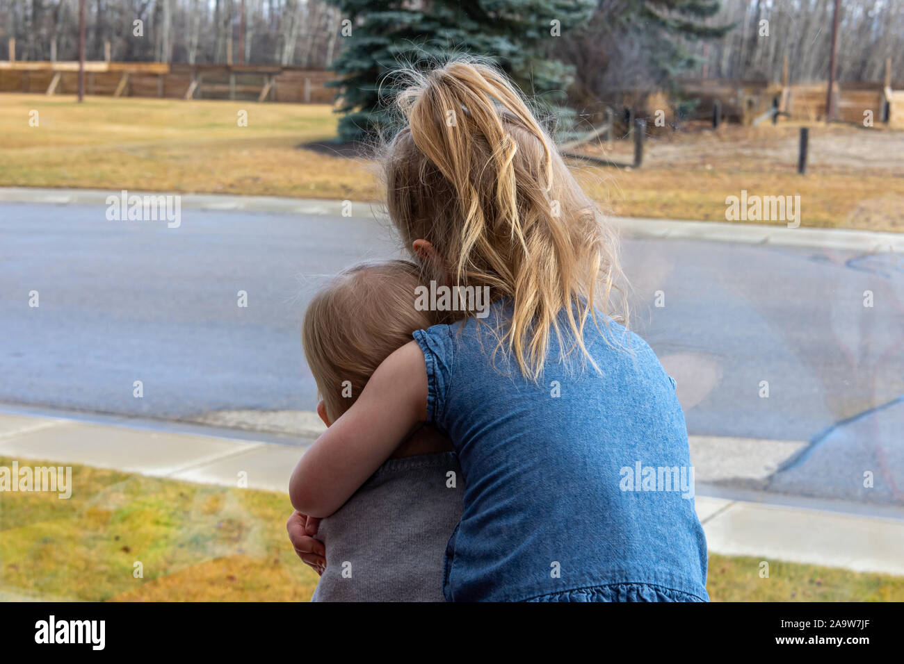 Ein junges Mädchen ihren Toddler Schwester halten, als Sie sich ein großes Fenster zu der Welt außerhalb. Stockfoto