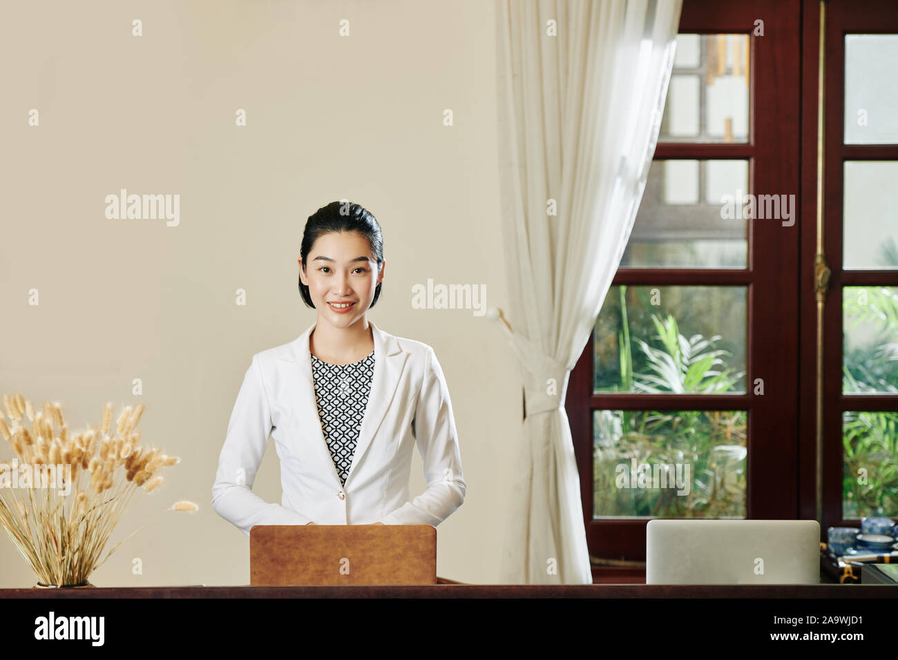 Junge schöne Vietnamesin in weisse Jacke auf dem Laptop an der Rezeption arbeiten Stockfoto
