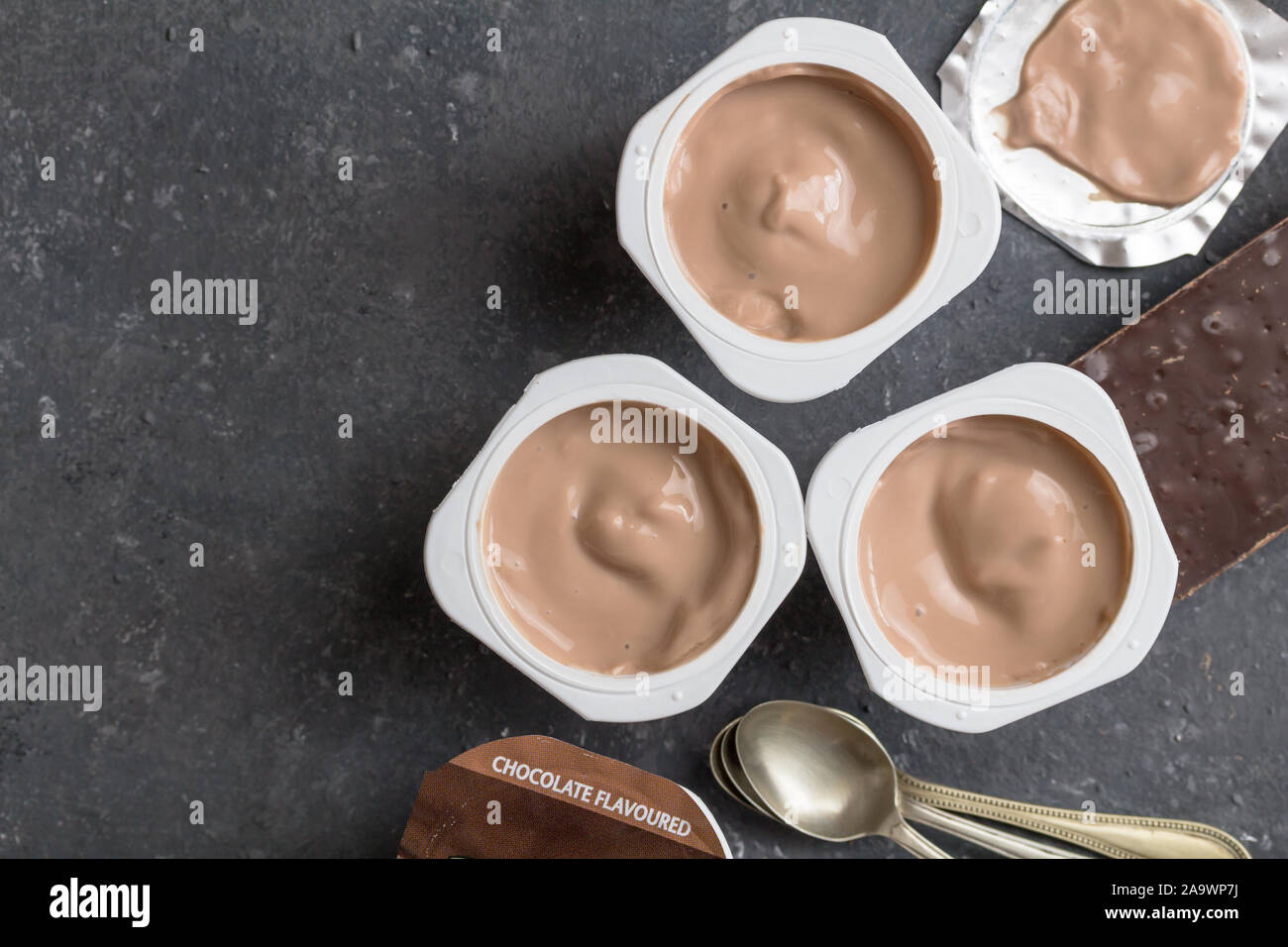 Schokolade Joghurtbecher auf schwarz-grau meliert Hintergrund mit kleinen silbernen Löffel - Drei mit Schokoladegeschmack Joghurtbecher mit dunkler Schokolade auf Stockfoto